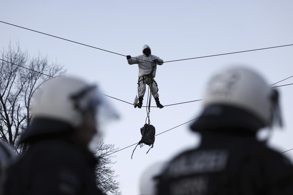 Police officers stay next to an activst who stands on a taut wire rope at the village Luetzerath near Erkelenz, Germany, Friday, Jan. 13, 2023. Police have entered the condemned village in to evict the climate activists holed up at the site in an effort to prevent its demolition, to make way for the expansion of a coal mine. (Rolf Vennenbernd/dpa via AP)