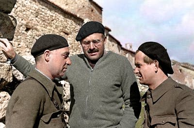 Two men dressed as soldiers talk face to face with a third man in the middle, wearing a beret.