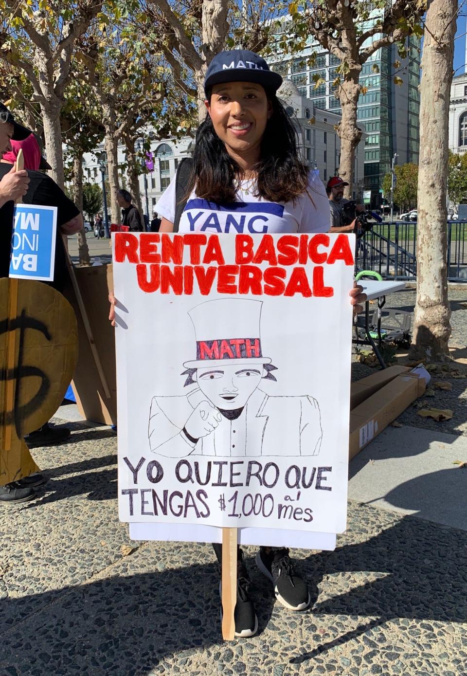 Eliana Jaramillo holds a sign in support of Democratic presidential candidate Andrew Yang's proposal for a universal basic income, which would grant everyone $1,000 a month to help cover basic expenses. She says this sort of monthly stipend would have helped her and her young children leave an abusive relationship sooner.