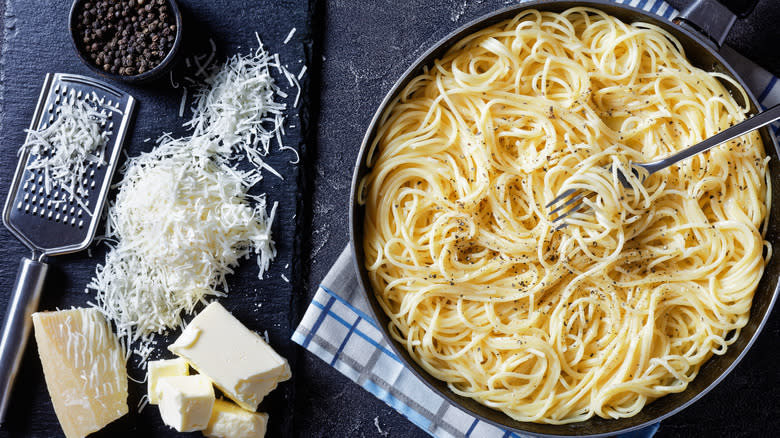 Cacio e pepe next to Parmesan and black peppercorns