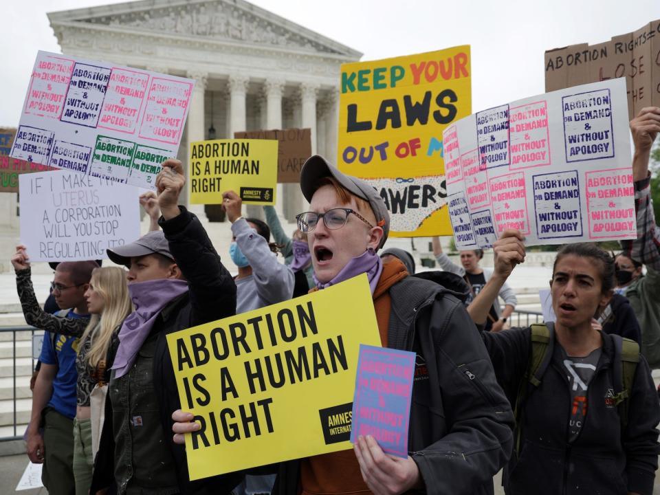 A group of abortion rights activists, some hoisting homemade signs aloft that read "Abortion is a human right." protest the looming reversal of Roe v. Wade on the steps of the Supreme Court.