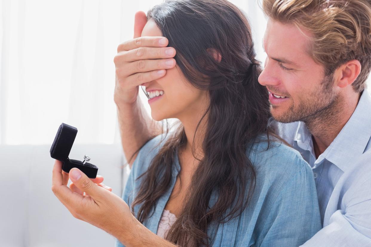 man hiding his wife's eyes to offer her an engagement ring for a marriage proposal