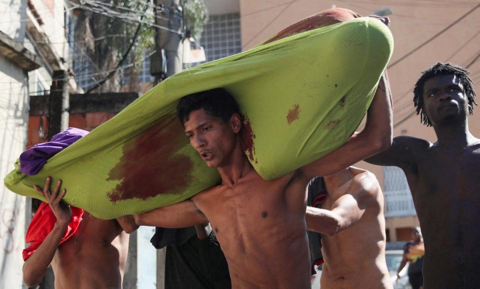 People carry a dead body during a police operation against drug gangs in the Alemao slums complex (Reuters)