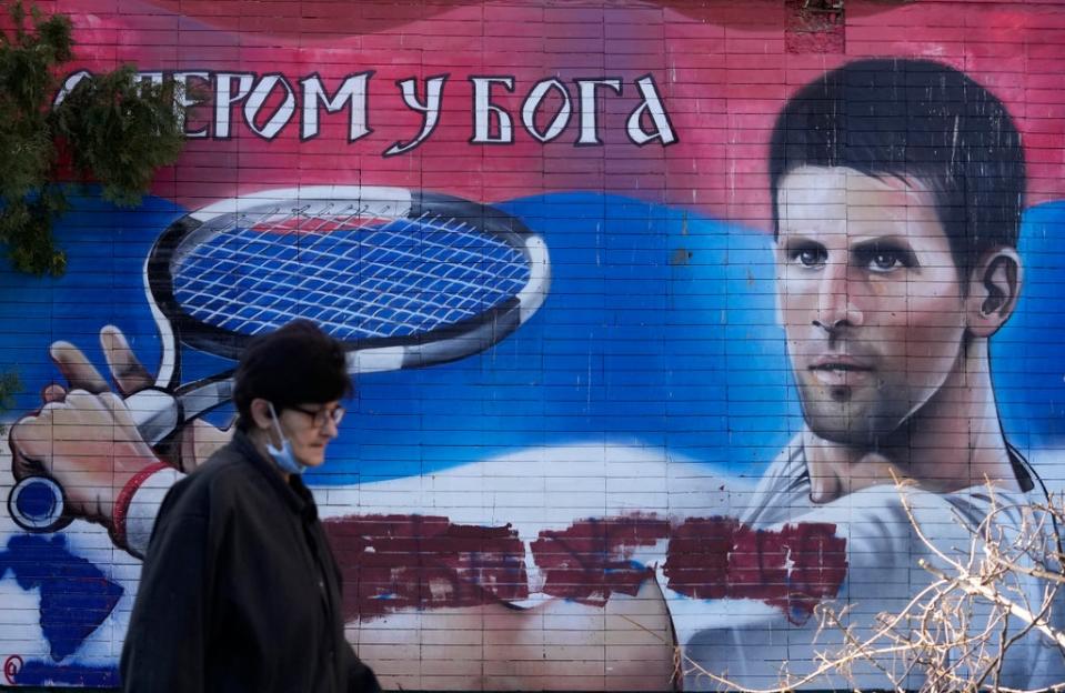 A woman passes a mural depicting Serbian tennis player Novak Djokovic, reading: “With faith in God” on a wall in Belgrade. Djokovic was deported from Australia on Sunday after failing to overturn the decision to cancel his visa (Darko Vojinovic/AP) (AP)