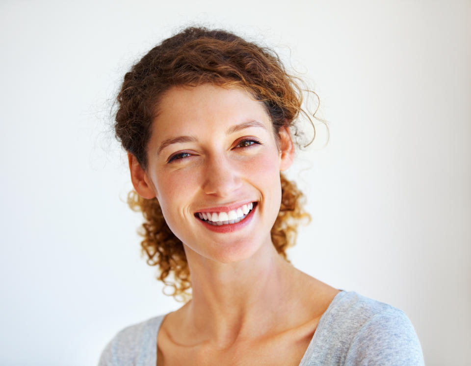 Woman with curly brunette hair in front of a white background smiling