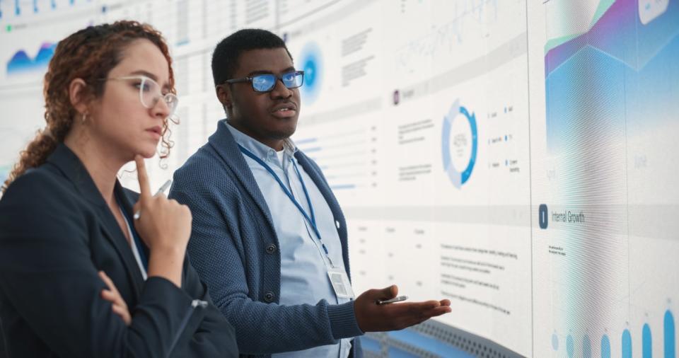 Two employees analyzing data on a huge screen. 