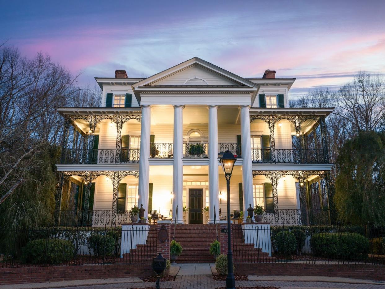 A large, white mansion lit up at sunset.