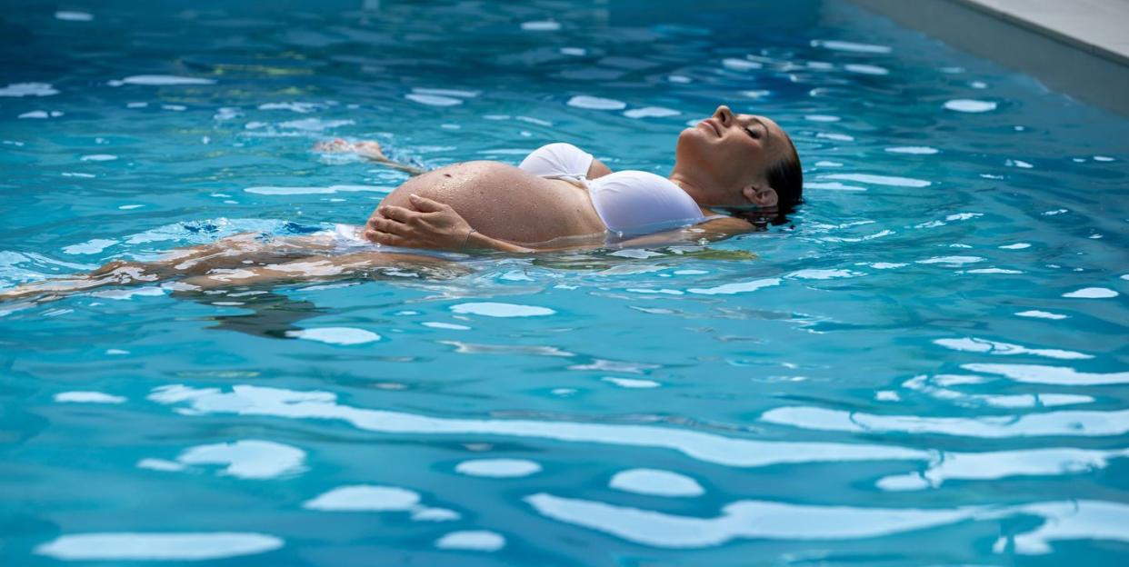 a woman in a pool with a pregnant stomach to illustrate a guide to the best maternity swimsuits 2023