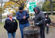 Striking United Auto Workers (UAW) members Melida Vela, Derrick Ventour and Roy Vermeulen warm their hands around a burn barrel while picketing outside the General Motors Detroit-Hamtramck Assembly in Hamtramck