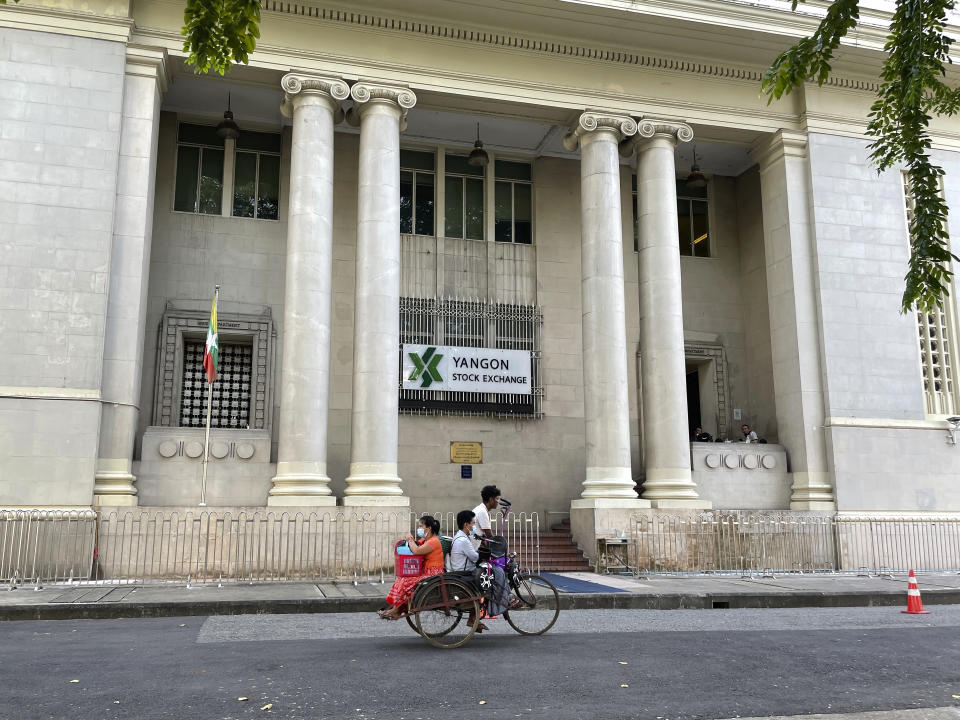 People onboard a trishaw pass in front of the Yangon stock exchange building in Kyauktada township in Yangon, Myanmar on Nov. 12, 2021. The military takeover in Myanmar has set its economy back years, if not decades, as political unrest and violence disrupt banking, trade and livelihoods and millions slide deeper into poverty. (AP Photo)