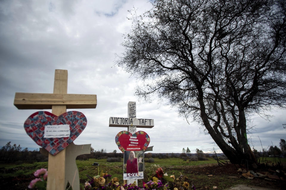 In this Feb. 8, 2019, photo, a cross for Victoria Taft, right, stands at a memorial for Camp Fire victims in Paradise, Calif. In the 100 days since a wildfire nearly burned the town of Paradise off the map, the long recovery is just starting. Work crews have been cutting down trees and clearing burned-out lots, but Paradise is mostly a ghost town where survivors still dig for keepsakes in the foundations of their homes. (AP Photo/Noah Berger)