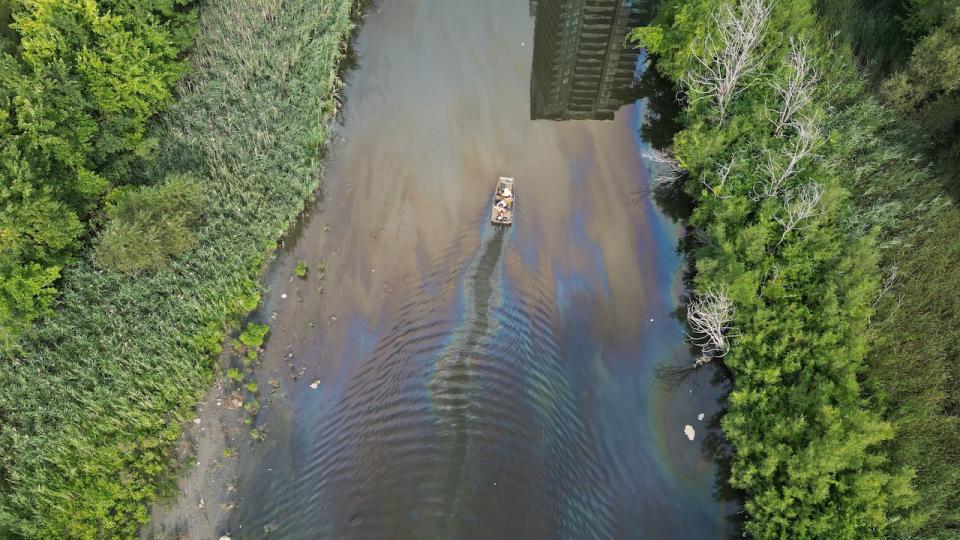 A drone view of Mimico Creek shows a boat skimming on the surface of the water. A sheen of oil is visible. 