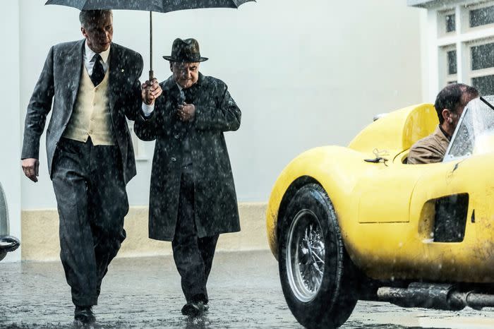 a man in a suit and tie walking next to a yellow car