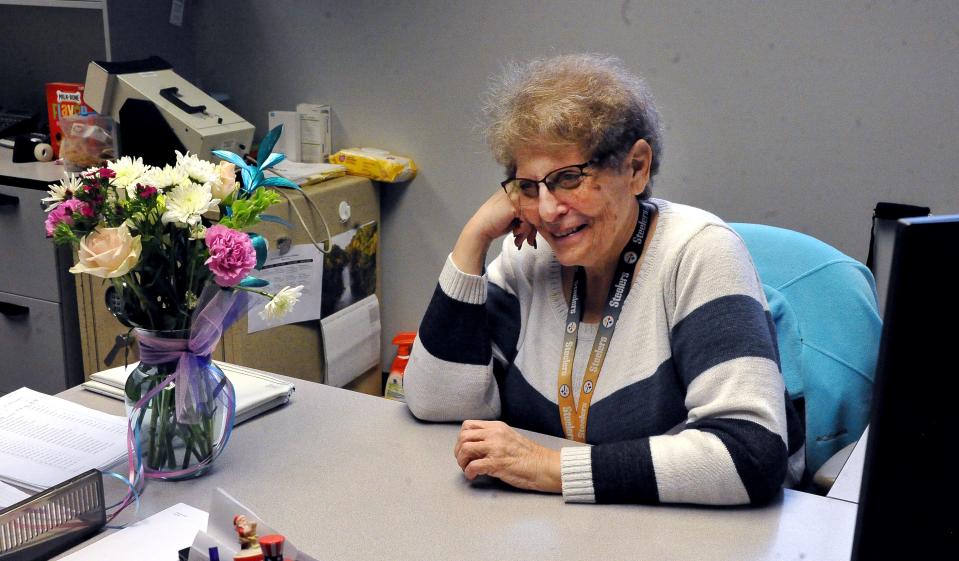 Bonnie Alfred sits at her desk in the Wayne County License Bureau with a floral boquet presented to her on her retirement after 45 years.