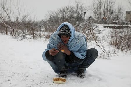 A migrant eats free food during a snowfall outside a derelict customs warehouse in Belgrade, Serbia January 9, 2017. REUTERS/Marko Djurica