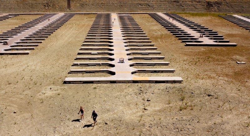 People walk near boat docks as they sit on dry land at the Browns Ravine Cove area of drought-stricken Folsom Lake in Folsom, California on May 22, 2021.