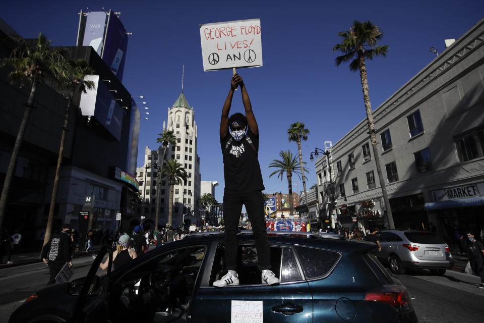 A demonstrator climbs on a car and holds a sign Sunday June, 7, 2020 in the Hollywood area of Los Angeles, during a protest over the death of George Floyd who died May 25 after he was restrained by Minneapolis police. (AP Photo/Marcio Jose Sanchez)