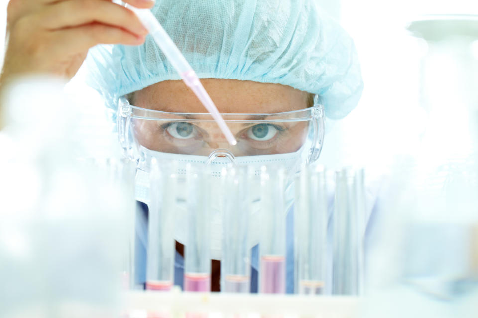 Lab employee pipetting pink liquid into test tubes.