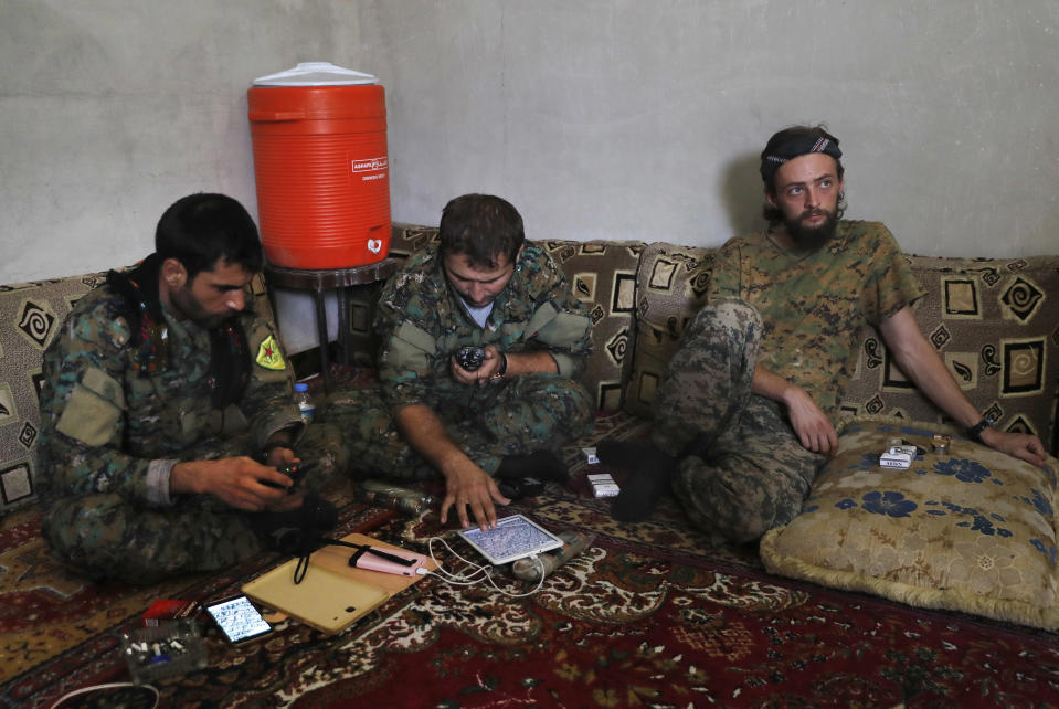 FILE -- In this July 18, 2017 file photo, a British man identified as Jac Holmes, right, who had been fighting with U.S.-backed Syrian Democratic Forces against Islamic State group, sits on the ground next to two Kurdish commanders at a front line base, in the northern city in Raqqa, Syria. Syria’s Kurds have been America’s partner in fighting the Islamic State group for nearly four years. Now they are furious over an abrupt U.S. troop pull-back that exposes them to a threatened attack by their nemesis, Turkey. The surprise U.S. pull-back from positions near the Turkish border, which began Monday, Oct. 7, 2019, stung even more because the Kurds have been abandoned before by the U.S. and other international allies on whose support they'd pinned their aspirations.. (AP Photo/Hussein Malla, File)