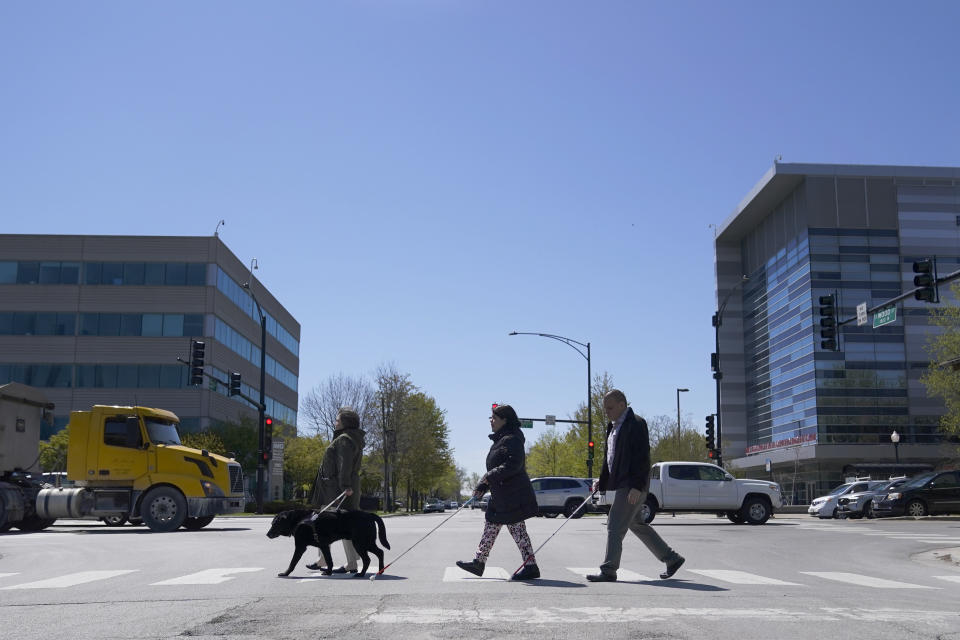 Maureen Reid, left, and her guide dog, Gaston, cross the intersection of Wood Street and Roosevelt Avenue with Sandy Murillo, center, and Geovanni Bahena, relying on an audible signal for the blind, on Wednesday, April 26, 2023, in Chicago. A federal court ruling slamming street crossing signals in Chicago as dangerous for blind and low-vision residents are giving momentum to advocates who say the community has long been left out of the push for safer streets. (AP Photo/Charles Rex Arbogast)
