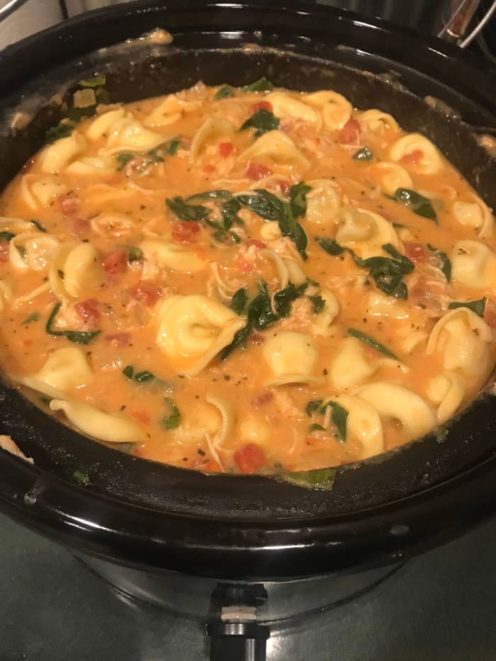 A slow cooker filled with creamy tortellini, spinach, diced tomatoes, and herbs