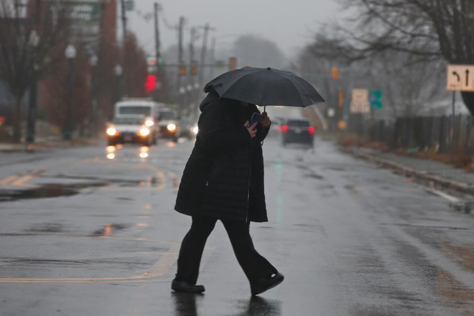 A woman crosses Coggeshall Street in New Bedford with an umbrella as heavy rain falls across the region