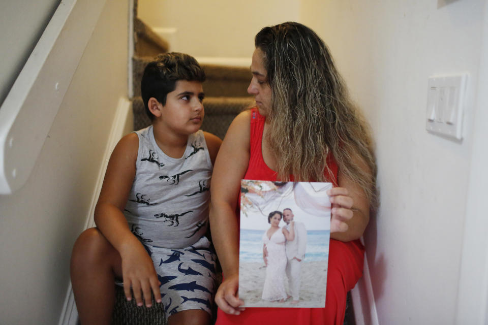 In this Aug. 6, 2019, photo, Barbara Rodriguez and her son, Nolan Aragon, 9, pose for a photograph in Hialeah, Fla. Rodriguez is holding a wedding photograph of her and her husband, Pablo Sanchez, who is currently in detention in the U.S. and is now facing deportation to Cuba. (AP Photo/Brynn Anderson)