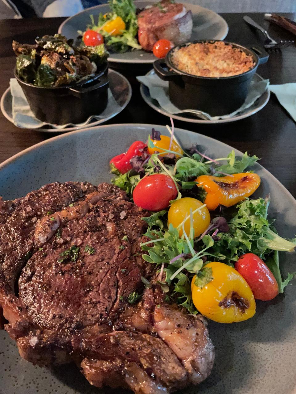 The 16-ounce ribeye at Fire + Smoke on Northshore Drive is plated with warm greens topped with different varieties of tomatoes and peppers.
