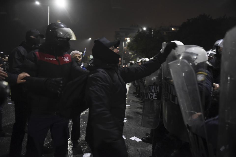 Hooded protesters gesture in front of riot police during a rally in the northern Greek city of Thessaloniki, Friday, Dec. 14, 2018. Hundreds of people protest against government efforts to end a three-decade-old dispute with neighboring Macedonia as the Greek Prime Minister Alexis Tsipras will deliver a speech to party cadres and supporters. (AP Photo/Giannis Papanikos)