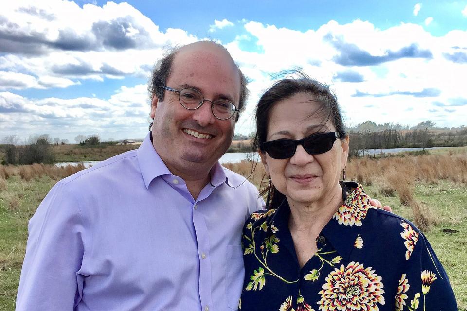 A middle-aged white man with glasses and a middle-aged woman with dark hair stand side by side in a field.