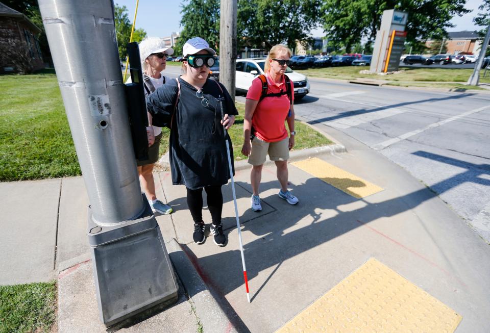 Madison Smith, a teacher in Nashville, Tn., presses a crosswalk button as he navigates an intersection using a cane while wearing a pair of low vision simulators, designed to simulate visual conditions visually impaired people experience, with help from Stephanie Davison during a course for educators to learn how to better work with blind and visually-impaired students on Tuesday, June 27, 2023.