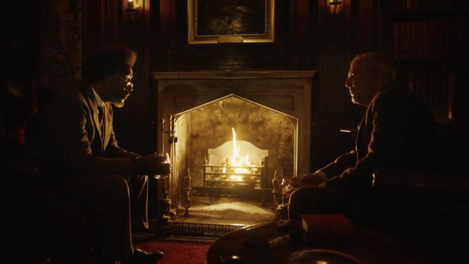The Master and Lyra's teacher talk in front of a fire place on His Dark Materials