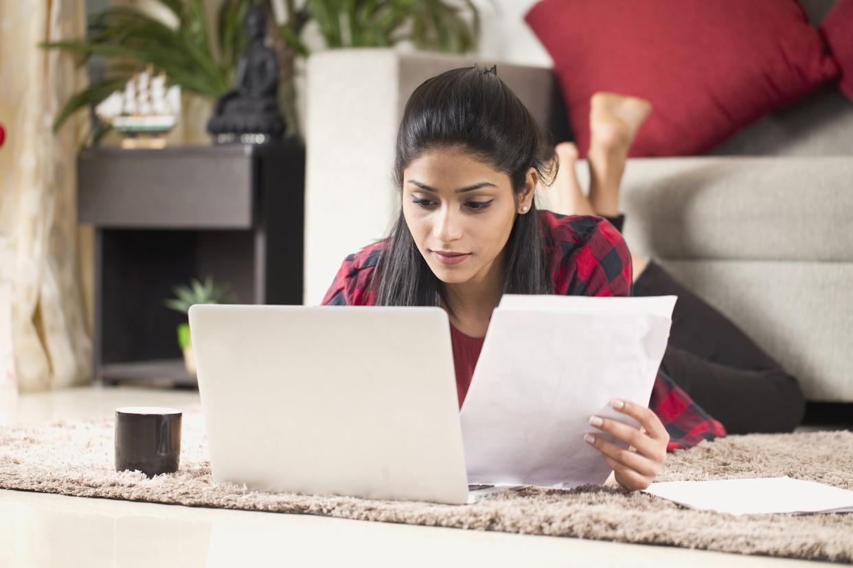 woman laying on floor of living room with laptop and papers