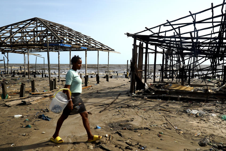 A woman walks past a stilt house that was damage due to coastal erosion in Ayetoro, Southwest Nigeria, Thursday, April 4, 2024. Ayetoro, a coastal community more than 200 km southeast of Nigeria's business capital Lagos, has been experiencing coastal erosion for many years. But the changes have recently rapidly worsened with the community slumping into the Atlantic Ocean, leading to repeated displacements of households and businesses. (AP Photo/Dan Ikpoyi)