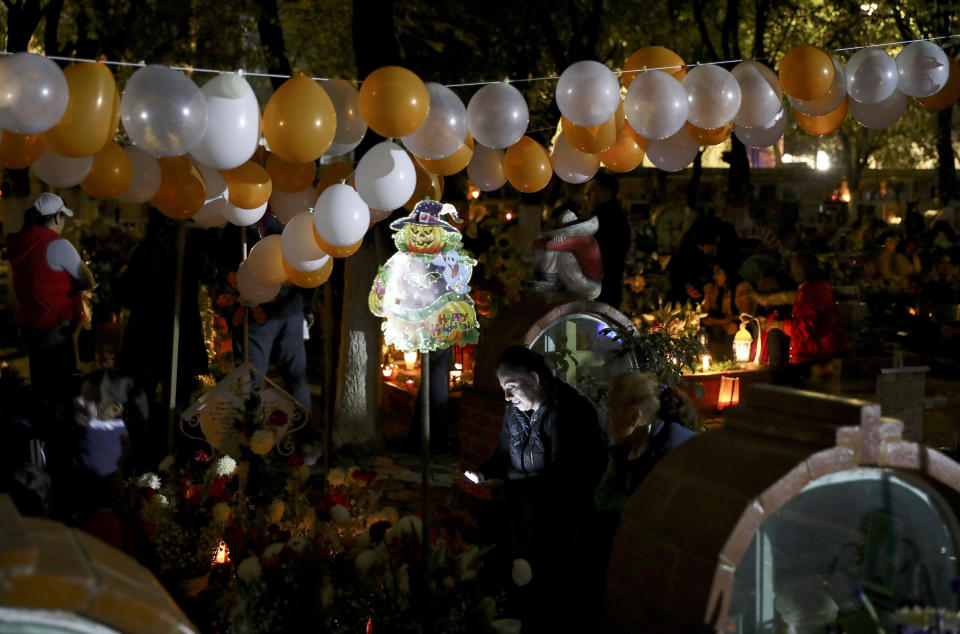 A relative spends the night next to the tomb of their loved one in the Los Reyes cemetery during Day of the Dead festivities in Mexico City, Friday, Nov. 1, 2019. In a tradition that coincides with All Saints Day and All Souls Day, families decorate the graves of departed relatives with flowers and candles, and spend the night in the cemetery, eating and drinking as they keep company with their deceased loved ones. (AP Photo/Eduardo Verdugo)