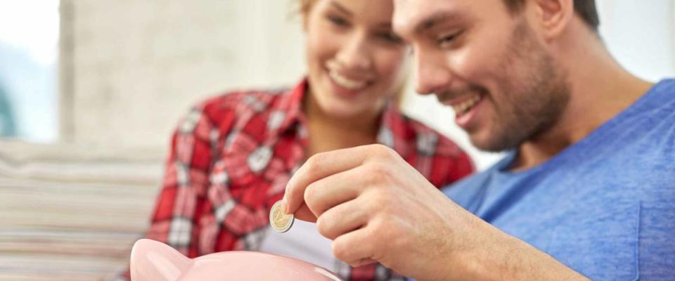 money, home, finance and relationships concept - close up of couple with piggy bank sitting on sofa