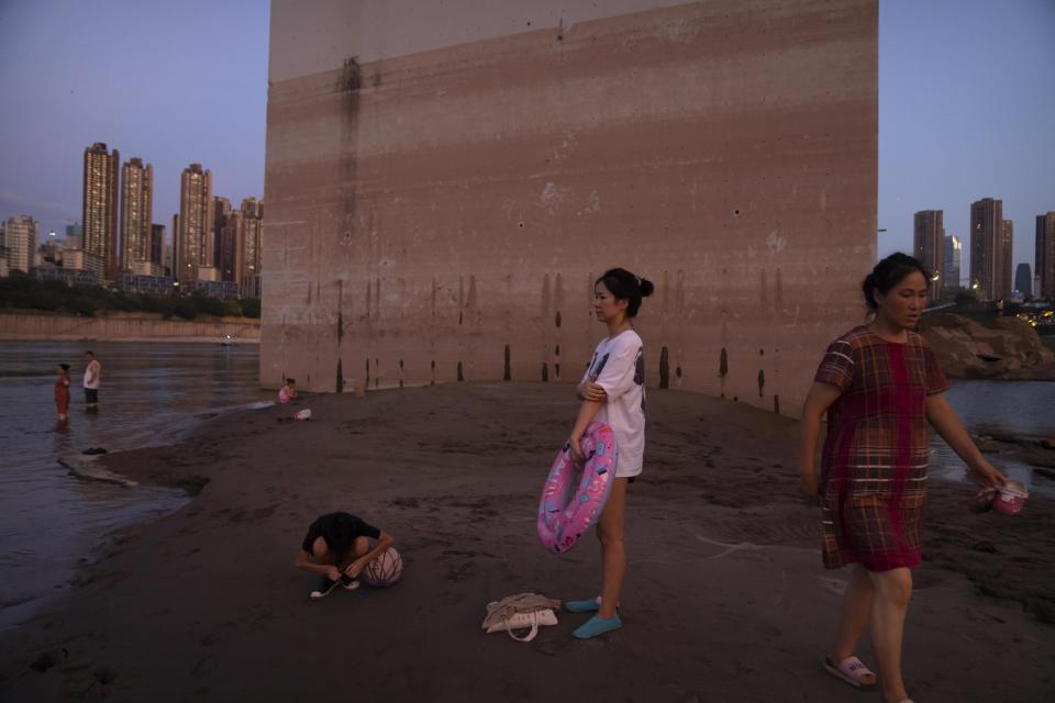 People prepare to swim in the Yangtze River near a bridge support column that shows previous water levels in southwestern China's Chongqing Municipality, Friday, Aug. 19, 2022. The very landscape of Chongqing, a megacity that also takes in surrounding farmland and steep and picturesque mountains, has been transformed by an unusually long and intense heat wave and an accompanying drought. (AP Photo/Mark Schiefelbein)