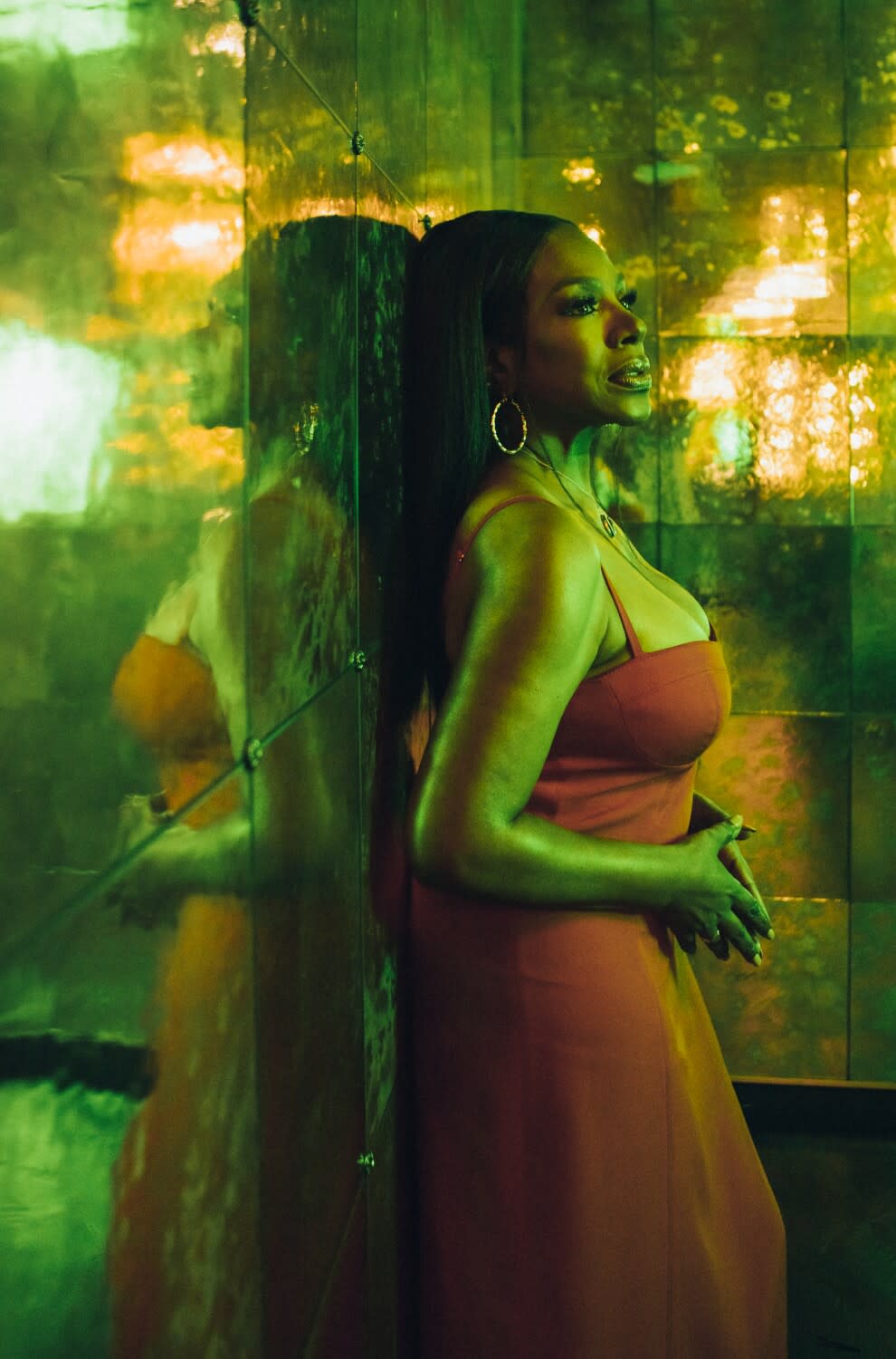 A woman in a red dress stands against a mirrored wall, back to back with her own reflection.