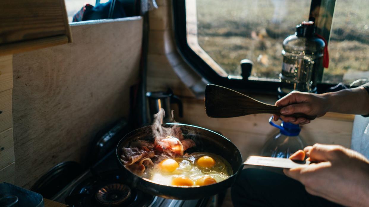 cooking eggs and bacon in skillet at campsite