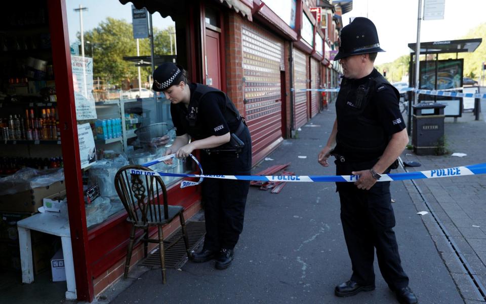 Police officers tie up cordon tape outside a barber's shop - Credit: DARREN STAPLES/Reuters