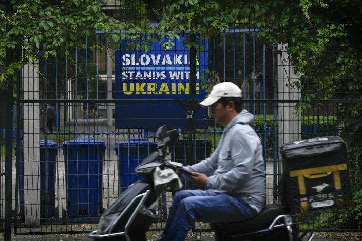 A delivery rider moves past a billboard showing a support for Ukraine on display in between fences at the Slovakia Embassy in Beijing, Thursday, May 17, 2023. Embassies in Beijing have been asked by the Chinese government to avoid displaying propaganda after some raised Ukrainian flags or set up placards declaring support for Ukraine. (AP Photo/Andy Wong)