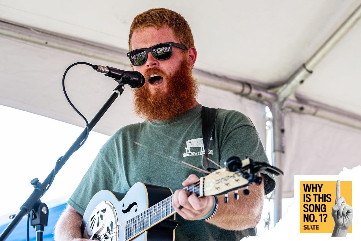 The red-headed singer performs under a tent in wayfarers, a bushy beard, and a green T-shirt with a small drawing of a cow and the word Goochland underneath.