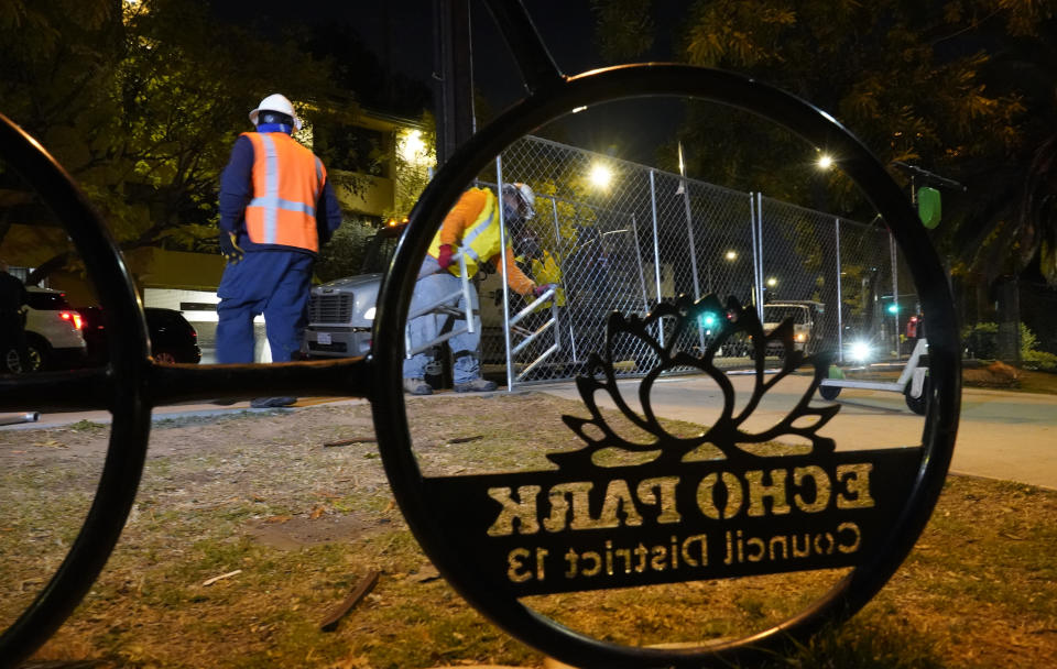 Los Angeles city contractors install a temporary fence around Echo Park Lake's perimeter in Los Angeles early Thursday, March 25, 2021. Los Angeles Police officers sweep managed to corral demonstrators gathered Wednesday to protest the planned closure of a Los Angeles park that would displace a large homeless encampment that has grown throughout the coronavirus pandemic. The park will be closed for repairs. (AP Photo/Damian Dovarganes)