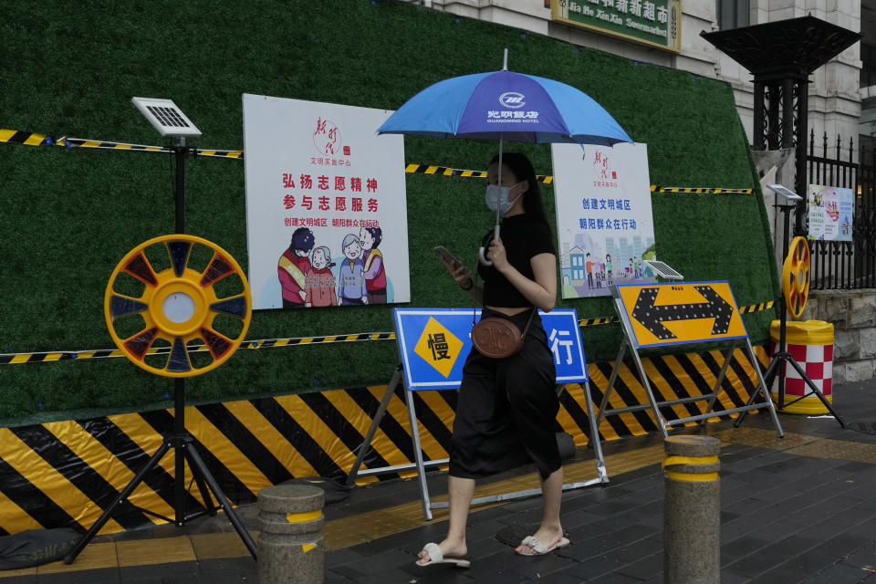 A woman wearing mask walks past construction warning sign during a rainy day in Beijing, Thursday, Aug. 18, 2022. Some were killed with others missing after a flash flood in western China Thursday, as China faces both summer rains and severe heat and drought in different parts of the country. (AP Photo/Ng Han Guan)