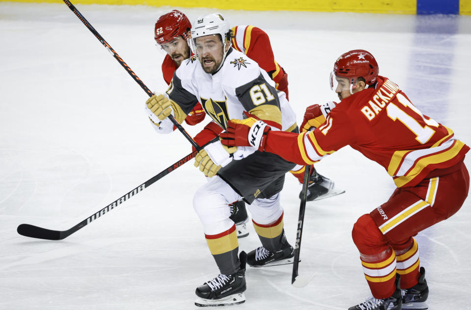 Vegas Golden Knights forward Mark Stone, center, is checked by Calgary Flames defenseman MacKenzie Weegar, left, and forward Mikael Backlund, right, during second-period NHL hockey game action in Calgary, Alberta, Monday, Nov. 27, 2023. (Jeff McIntosh/The Canadian Press via AP)