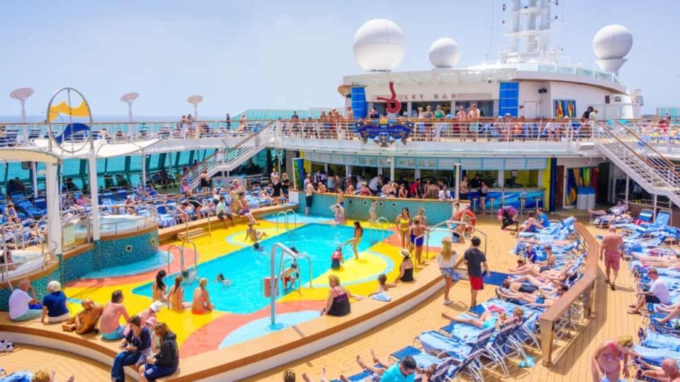 Cruise ship pool with people swimming and laying in deck chairs.