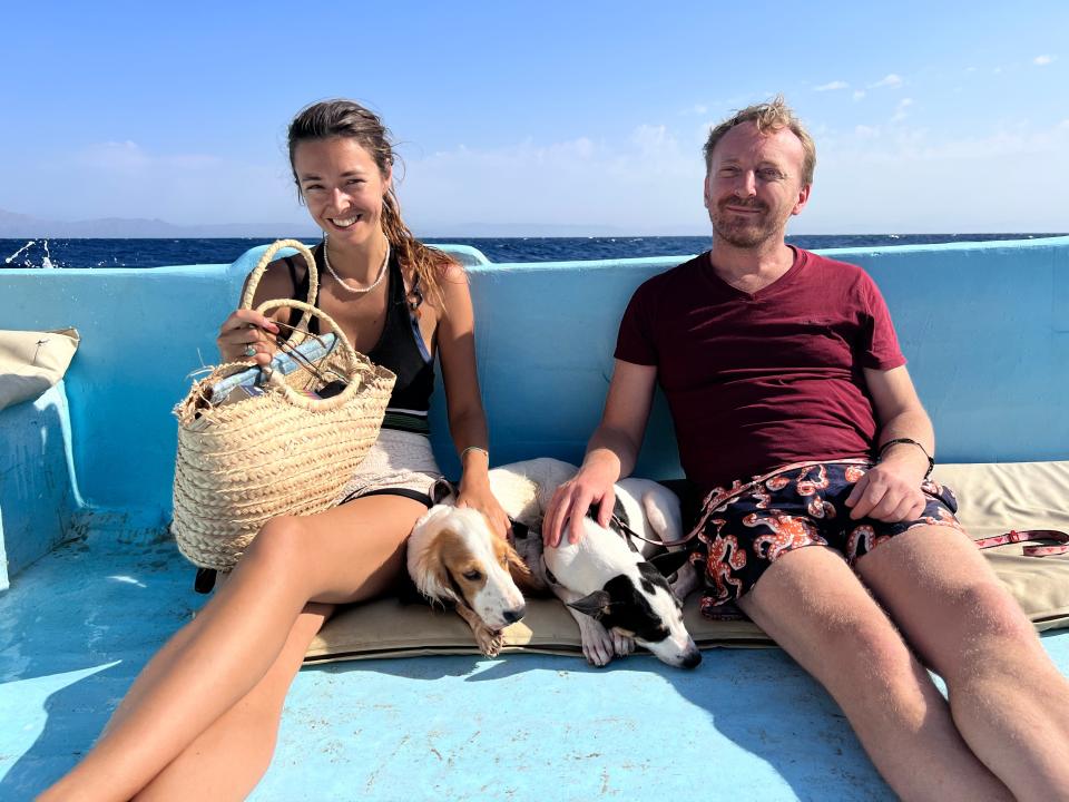 Lara Gibson and her husband Dan sitting on a boat and petting two dogs.