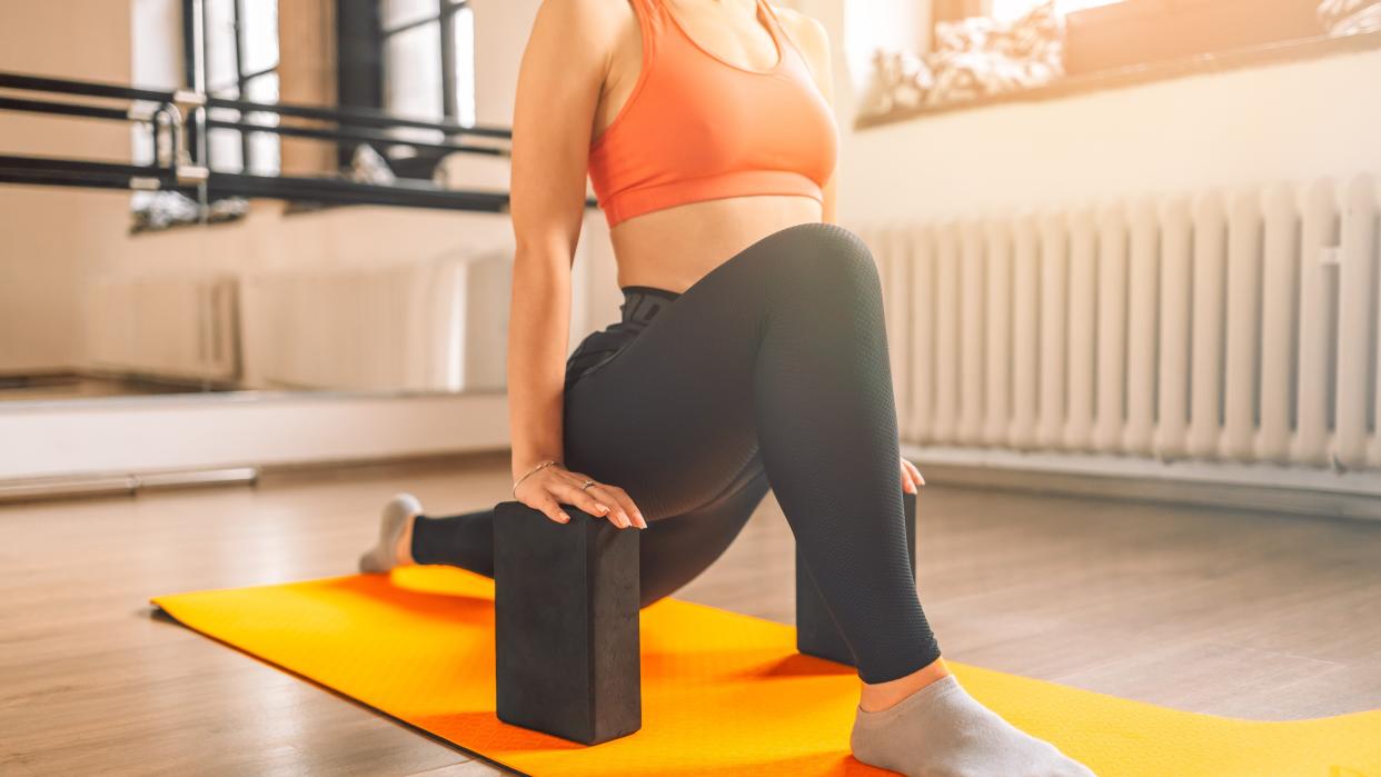  Woman performing a low lunge from shoulders down view and hands on blocks either side. 