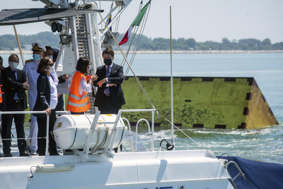 Italian Premier Giuseppe Conte, right, talks with Minister of Trasports and Infrastructures, Paola De Micheli, as Interior Minister Luciana Lamorgese, third from right, stand by them, aboard a Coast Guard ship in Venice, Italy, Friday, July 10, 2020. Venice has conducted a trial run an ambitious anti-flood system of 78 inflatable barriers in the hopes of protecting the lagoon city from devastating high tides. Premier Giuseppe Conte on Friday at a ceremony in Venice pressed a button that activated compressors to pump air into the bright yellow barriers, which then started rising from the sea to act a kind of a dike-on-demand. (Claudio Furlan/LaPresse via AP)