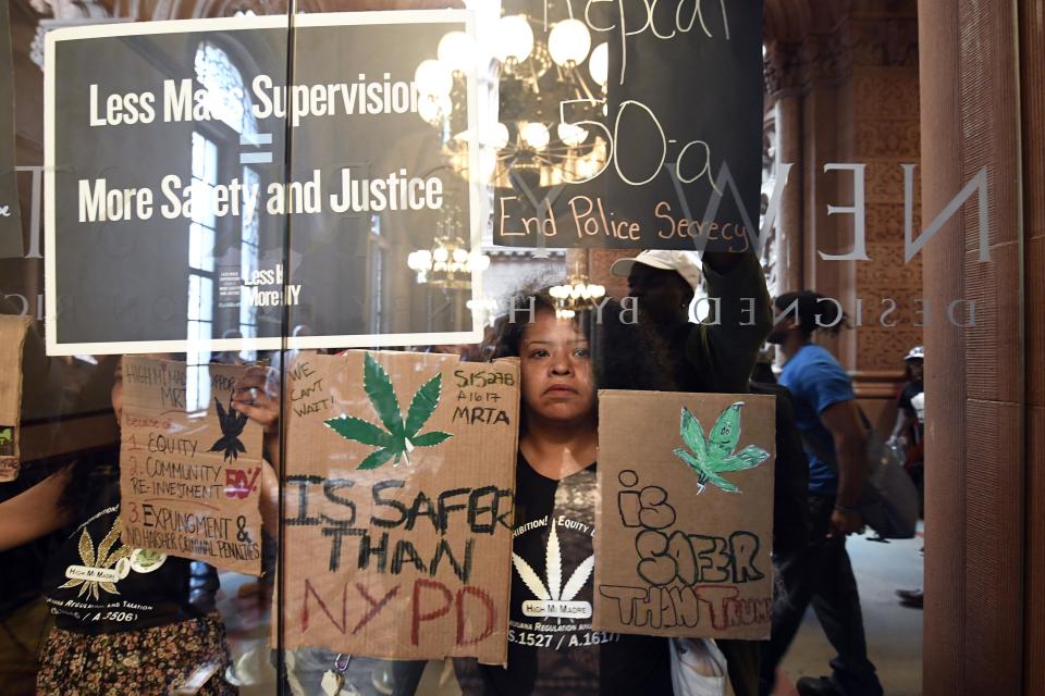 Pilar DeJesus with a coalition of protesters urging legislators to pass Marijuana legislation holds a sign against the senate lobby doors at the state Capitol Wednesday, June 19, 2019, in Albany, N.Y. (AP Photo/Hans Pennink)